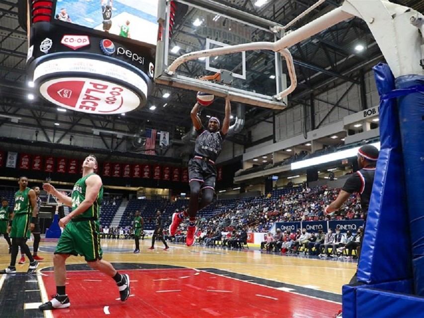 Basketball player mid-dunk in arena with spectators and ads in the background.