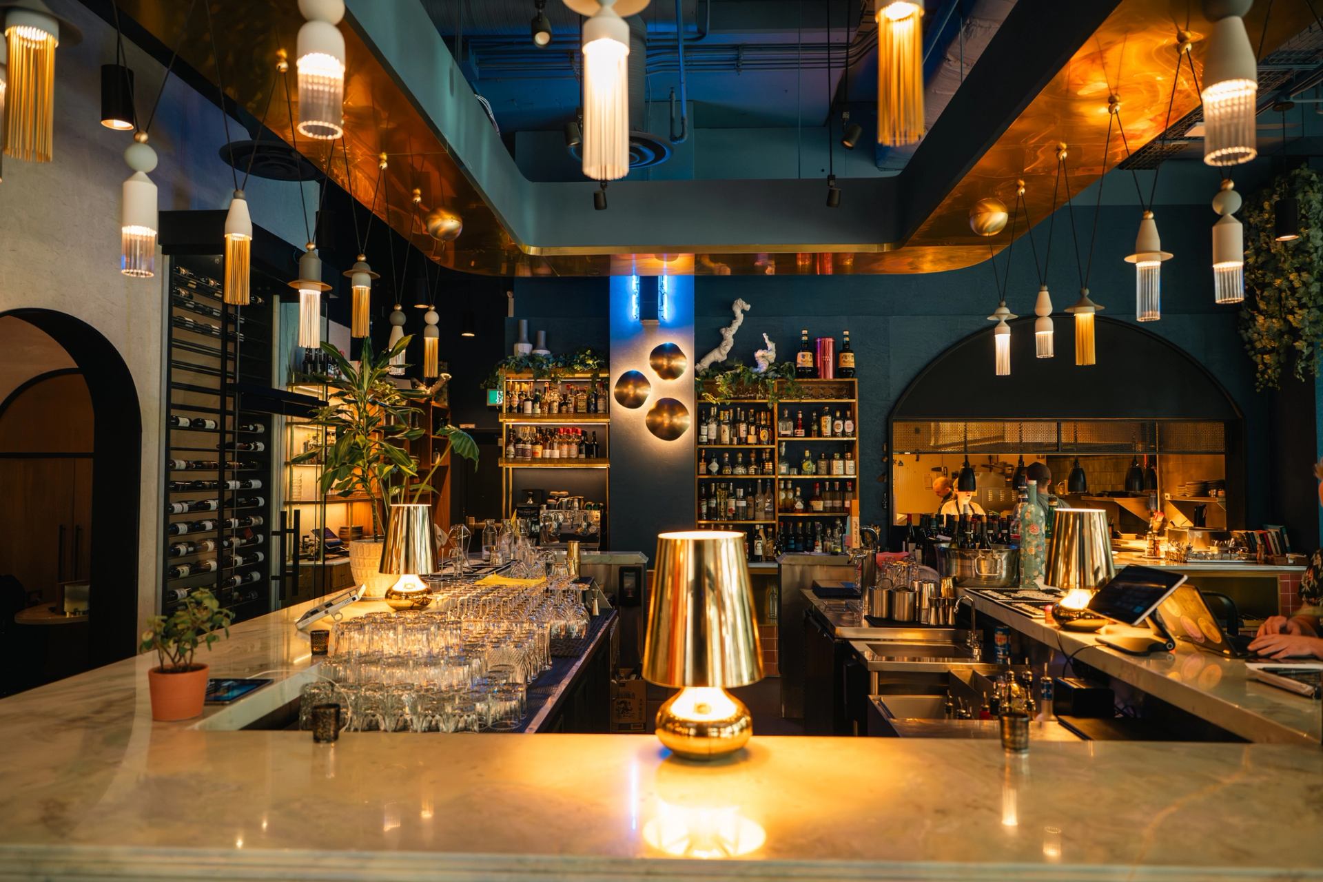 Modern cocktail bar interior with hanging lights, marble counter, glassware and liquor shelves.