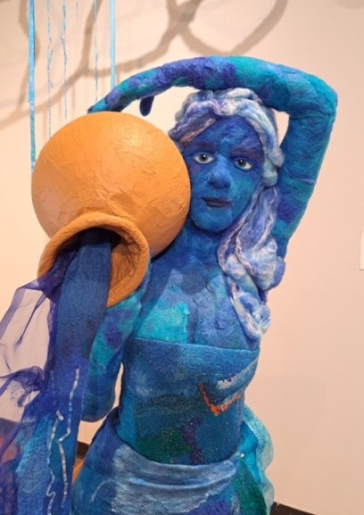 Blue sculptural figure holding a round vessel, representing water and movement.