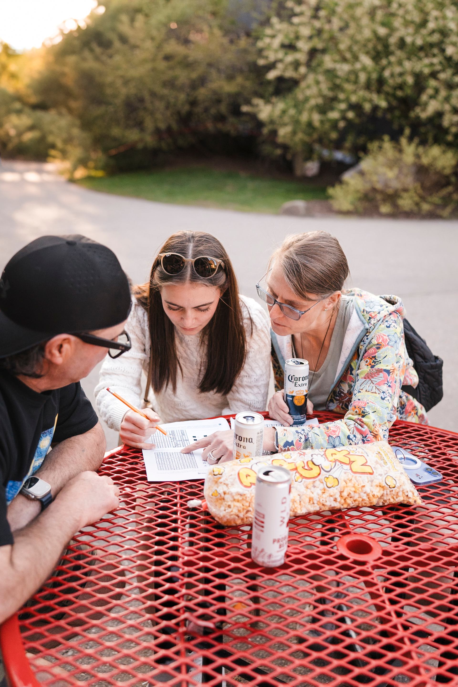 People sit at red picnic table, reviewing papers with drinks and popcorn.
