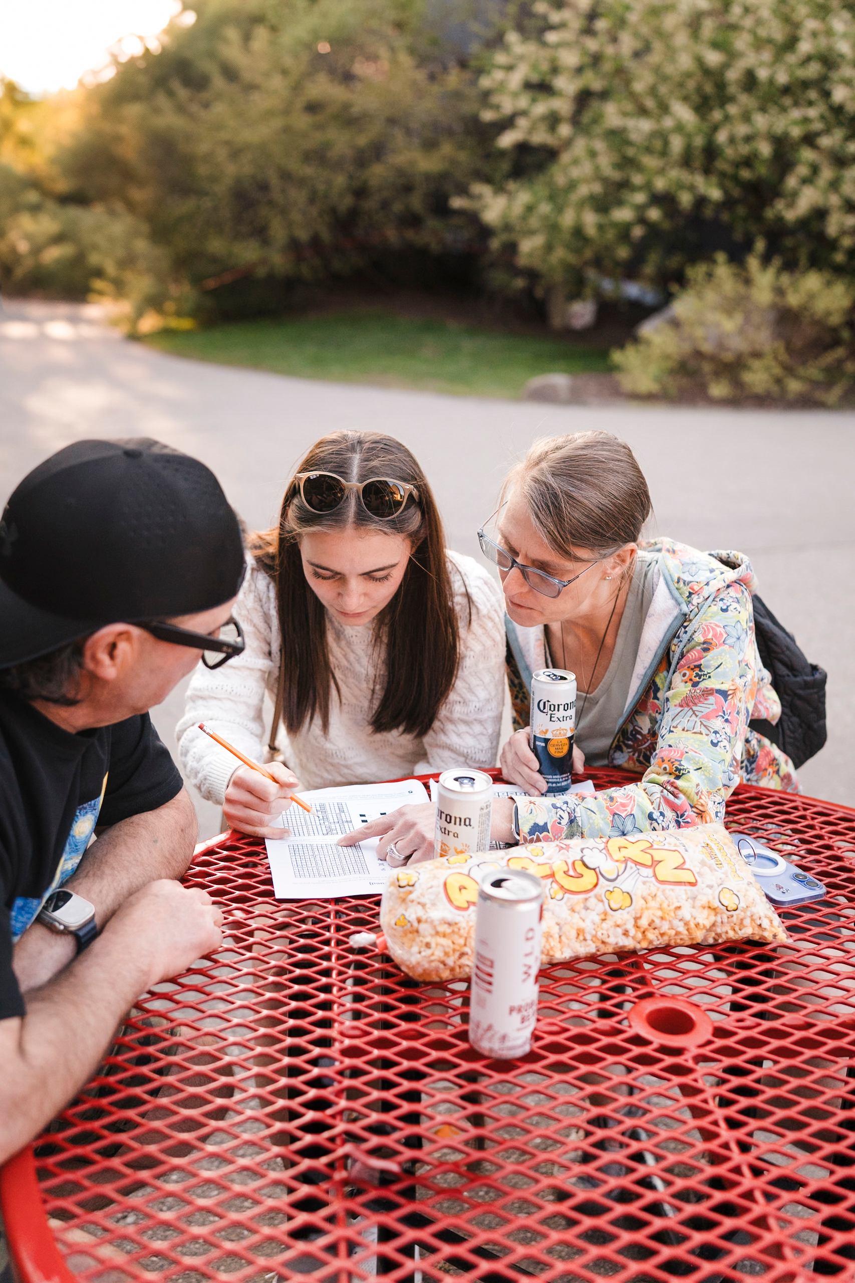 People sit at red picnic table, reviewing papers with drinks and popcorn.