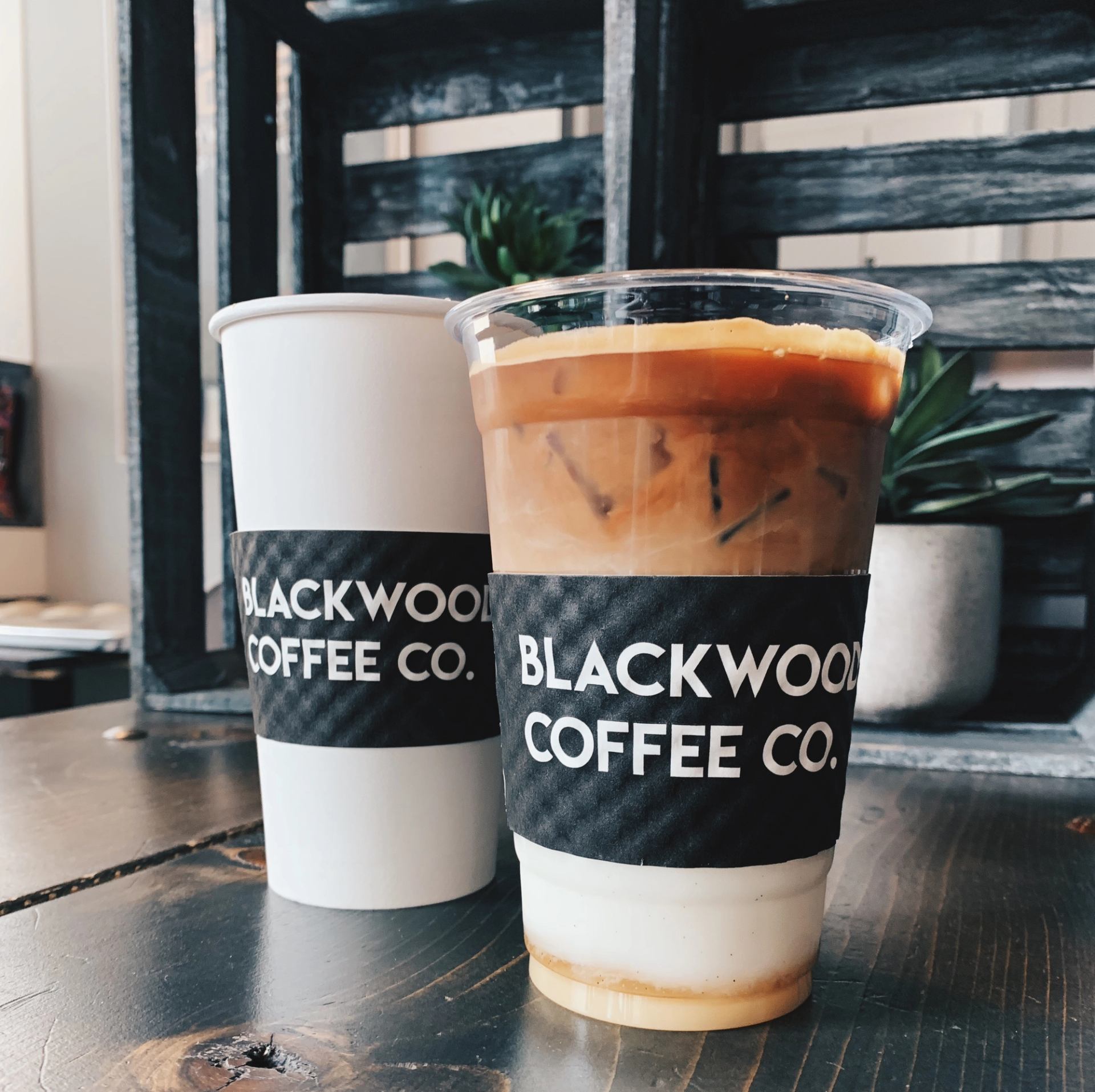 Two Blackwood Coffee Co. drinks on wooden table, one iced, one in white cup.