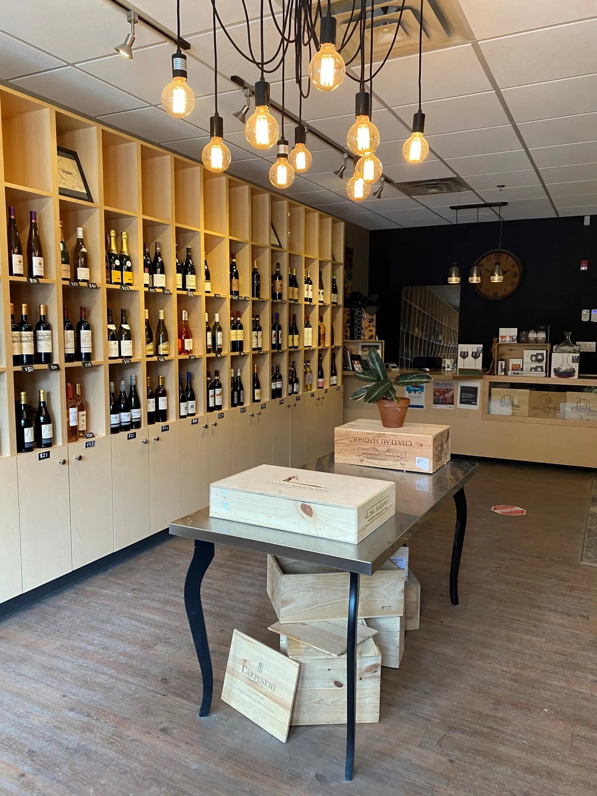 Wine shop interior with bottle wall, wooden crates on table, and hanging lights.
