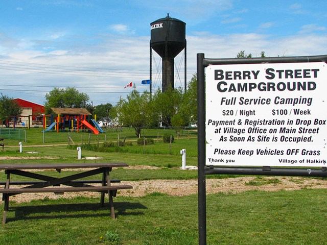Campground sign with picnic table and water tower in grassy park setting