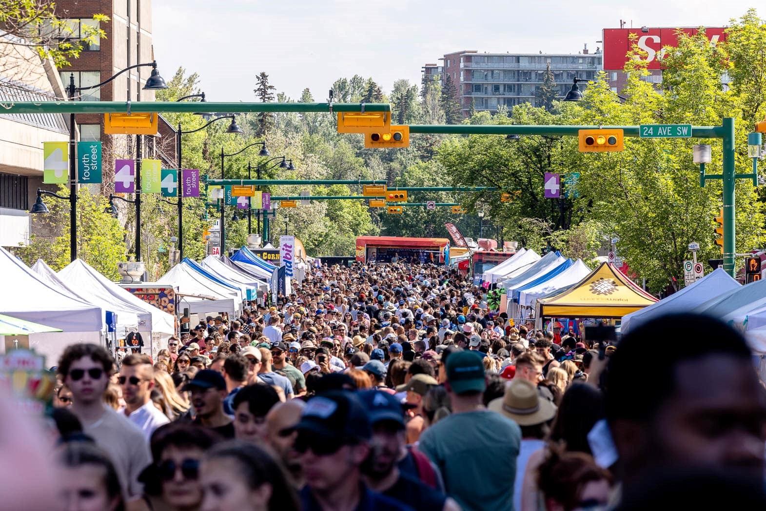 Crowded street lined with vendor tents and festival decorations on a sunny day.