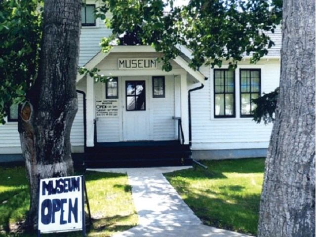 Museum building with sign reading “MUSEUM” and “MUSEUM OPEN” on walkway and lawn.