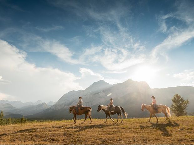 A group of people riding horses with the  Rocky Mountains in the background.