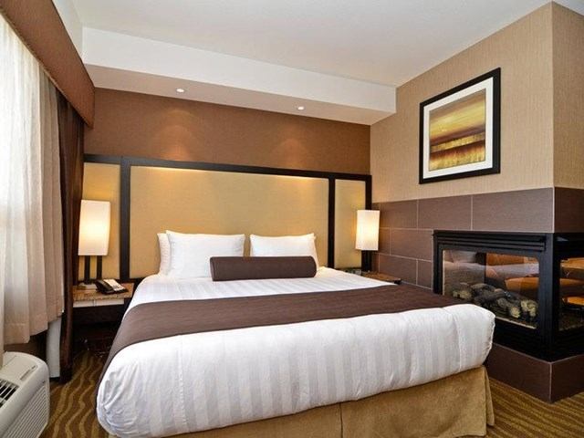 Modern hotel room with king bed, fireplace, and warm decor.