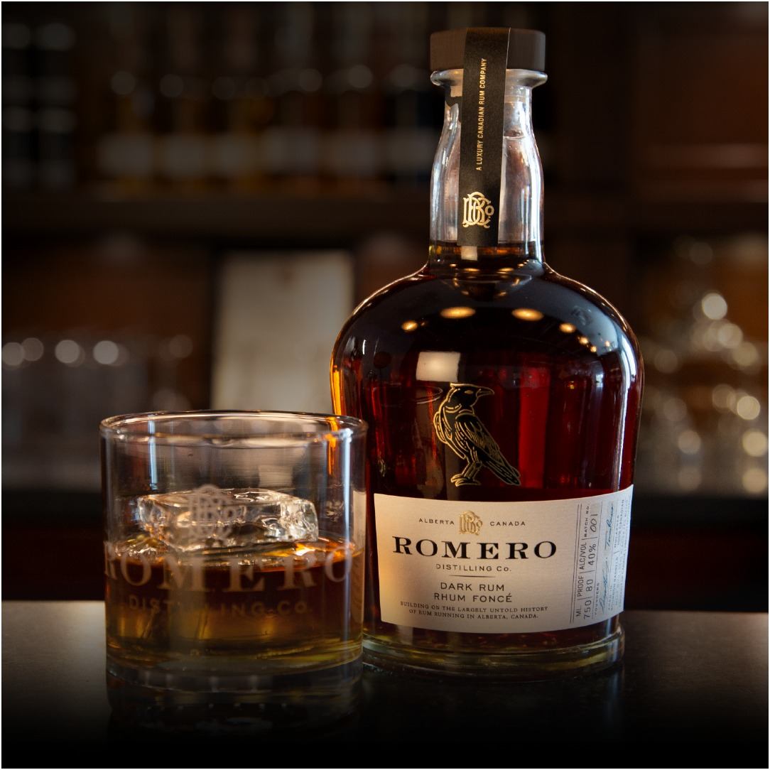 Romero Dark Rum bottle beside a glass of rum on ice on a bar surface
