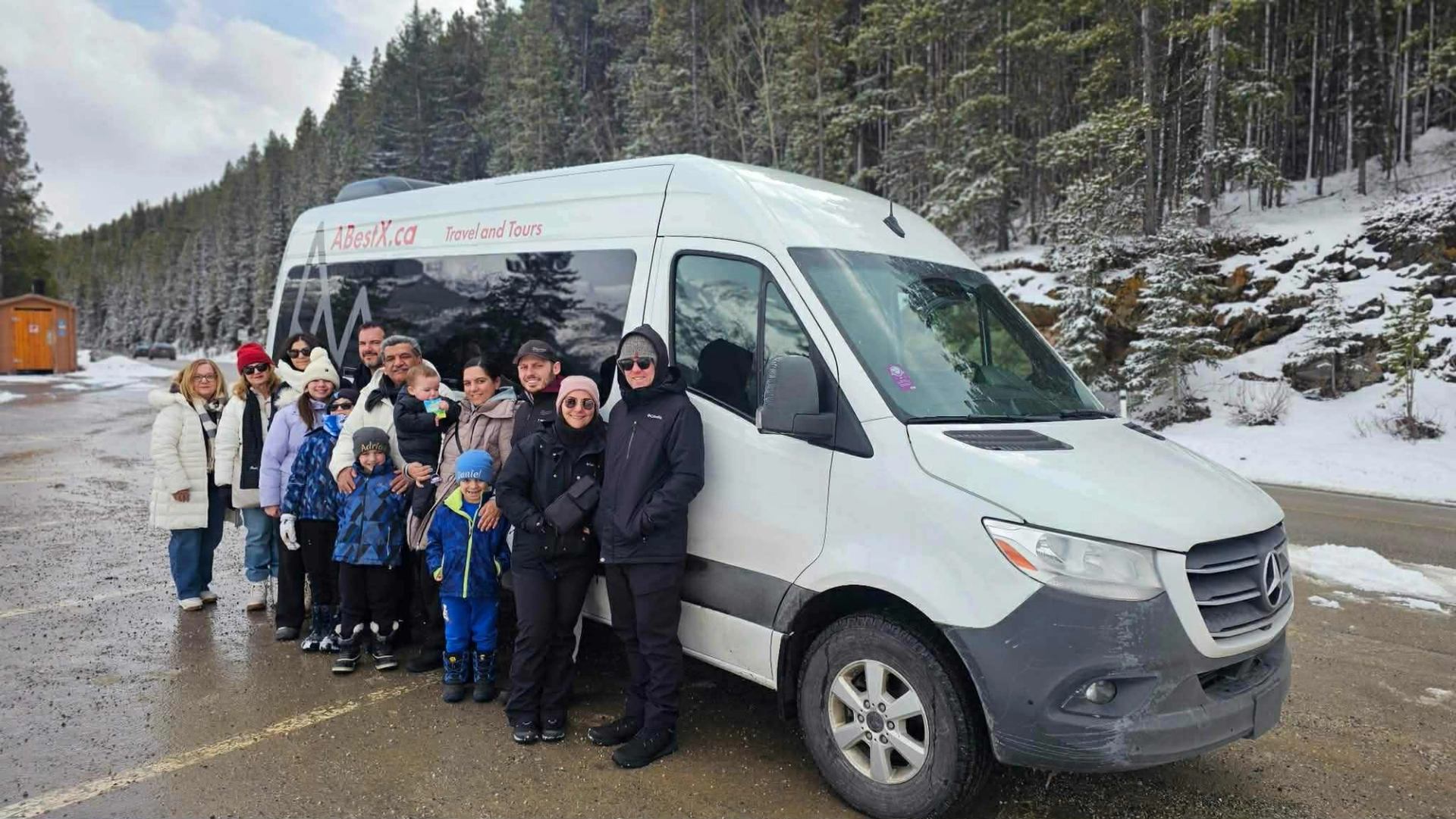 Group of people stand beside ABestX.ca tour van on snowy forest road.