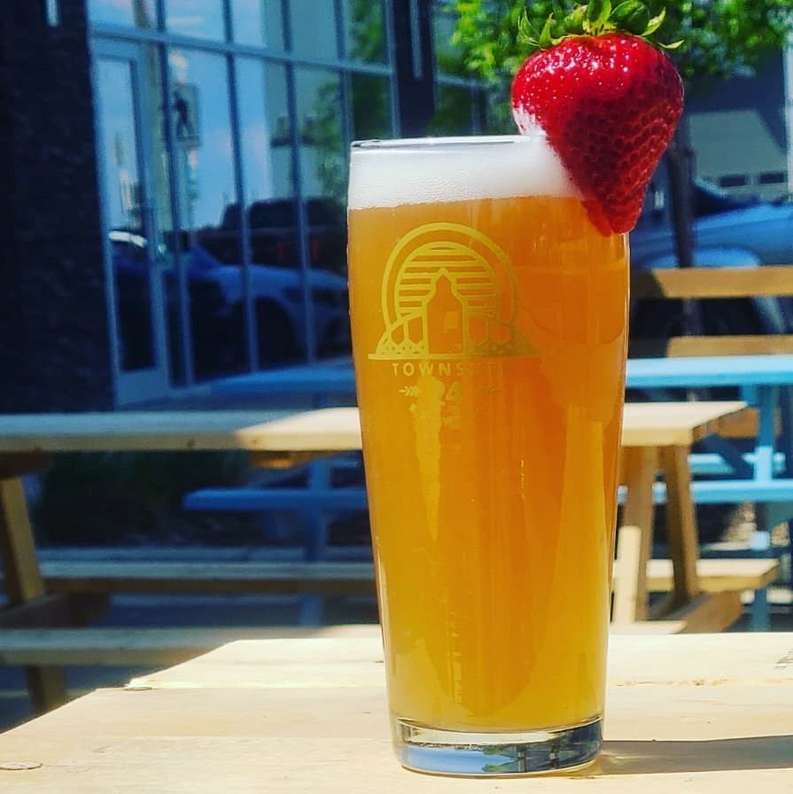 Glass of pale beer with strawberry garnish on a brewery patio table.