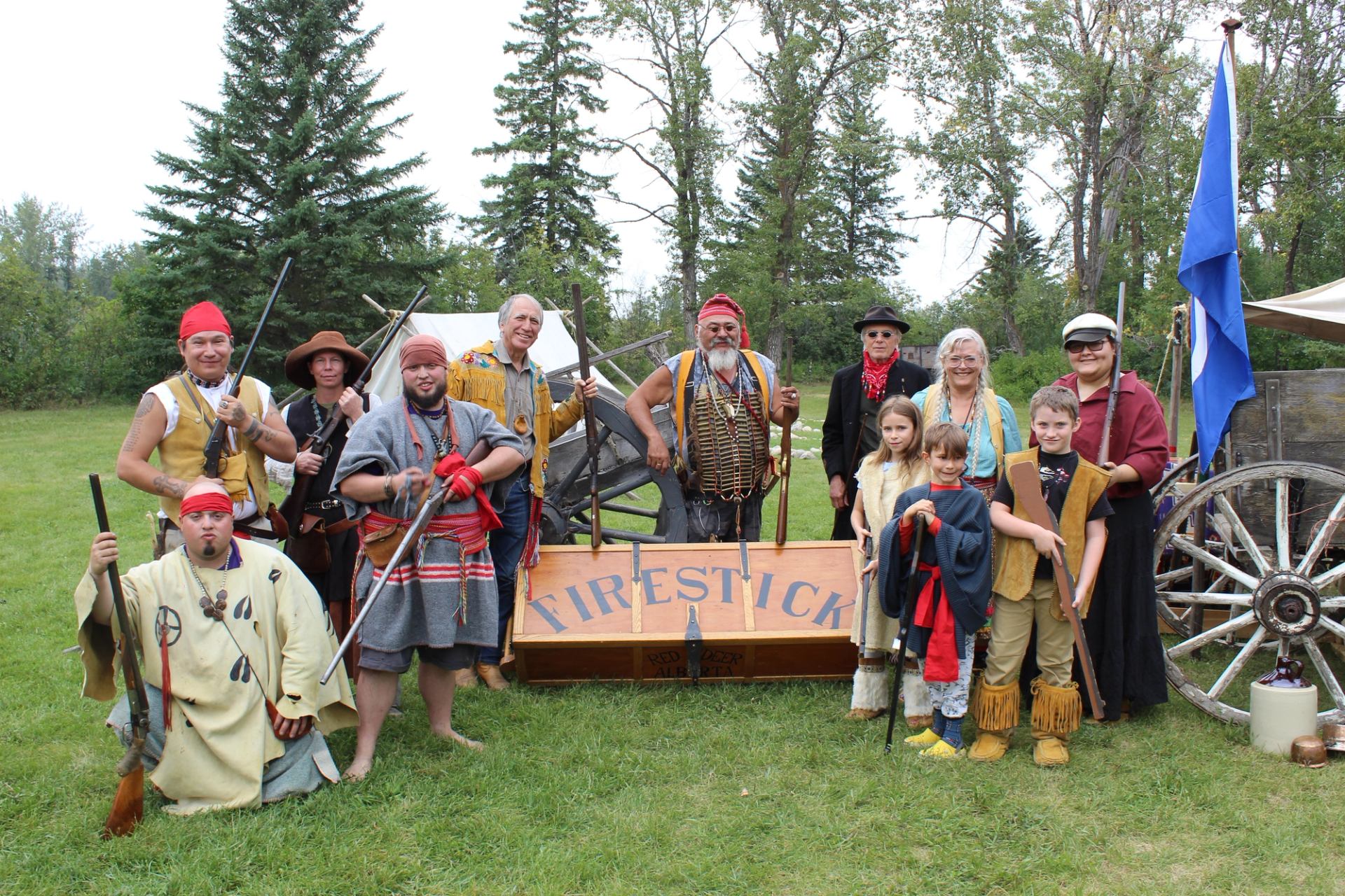 Costumed group poses with rifles, a wooden cart and a Firestick sign.