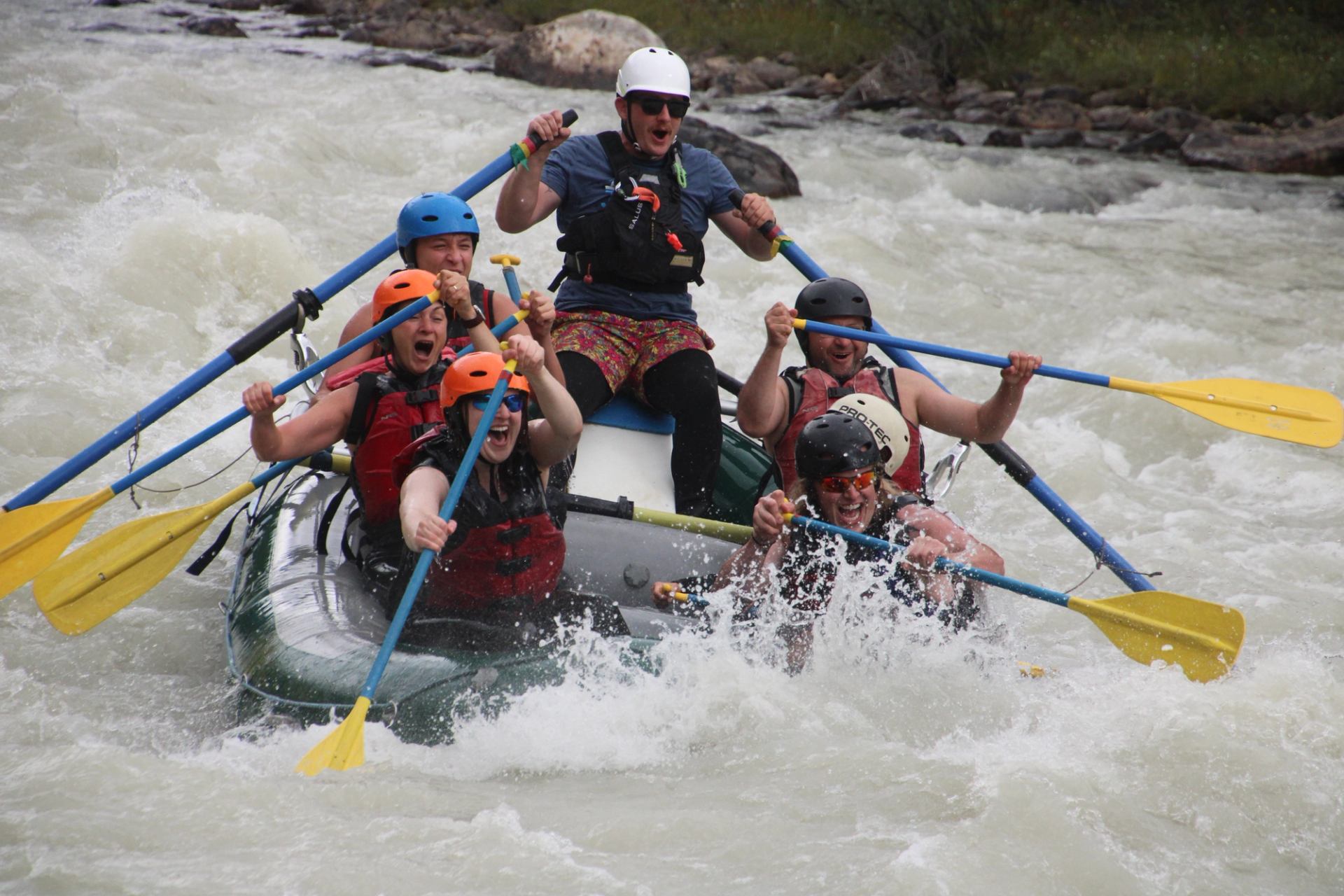 Rafting group hitting strong rapids, paddles raised as water splashes around them.