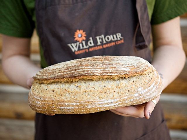 Fresh artisan loaf held by baker in Wild Flour Bakery apron.