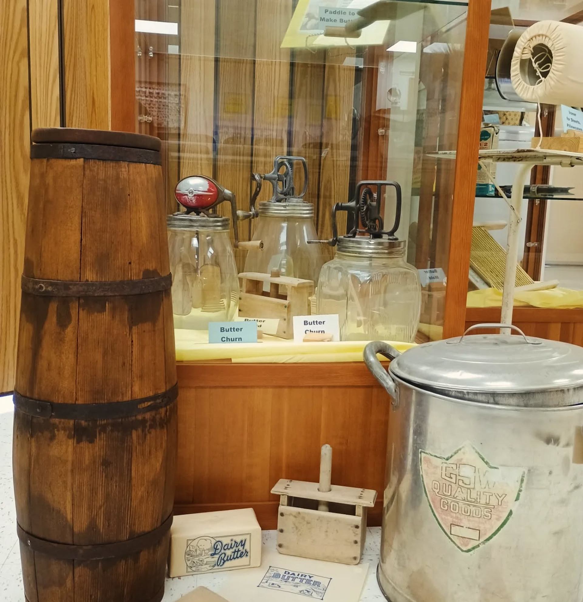 Wooden barrel, glass butter churns, and dairy tools in a museum case