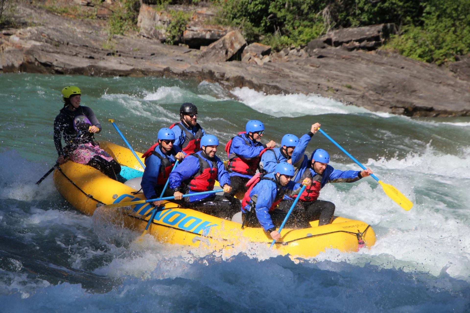 Group of rafters in helmets paddle yellow inflatable boat through whitewater rapids.