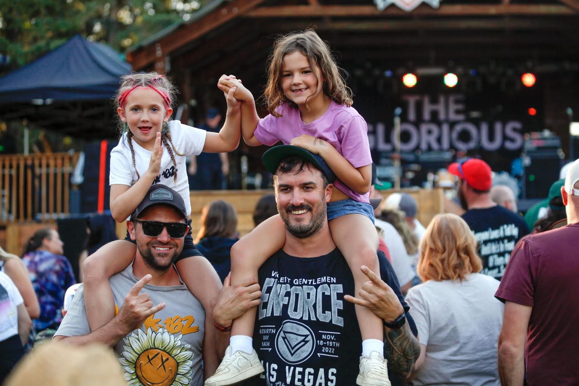 Adults carrying kids on their shoulders while enjoying an outdoor concert at Pigeon Lake.
