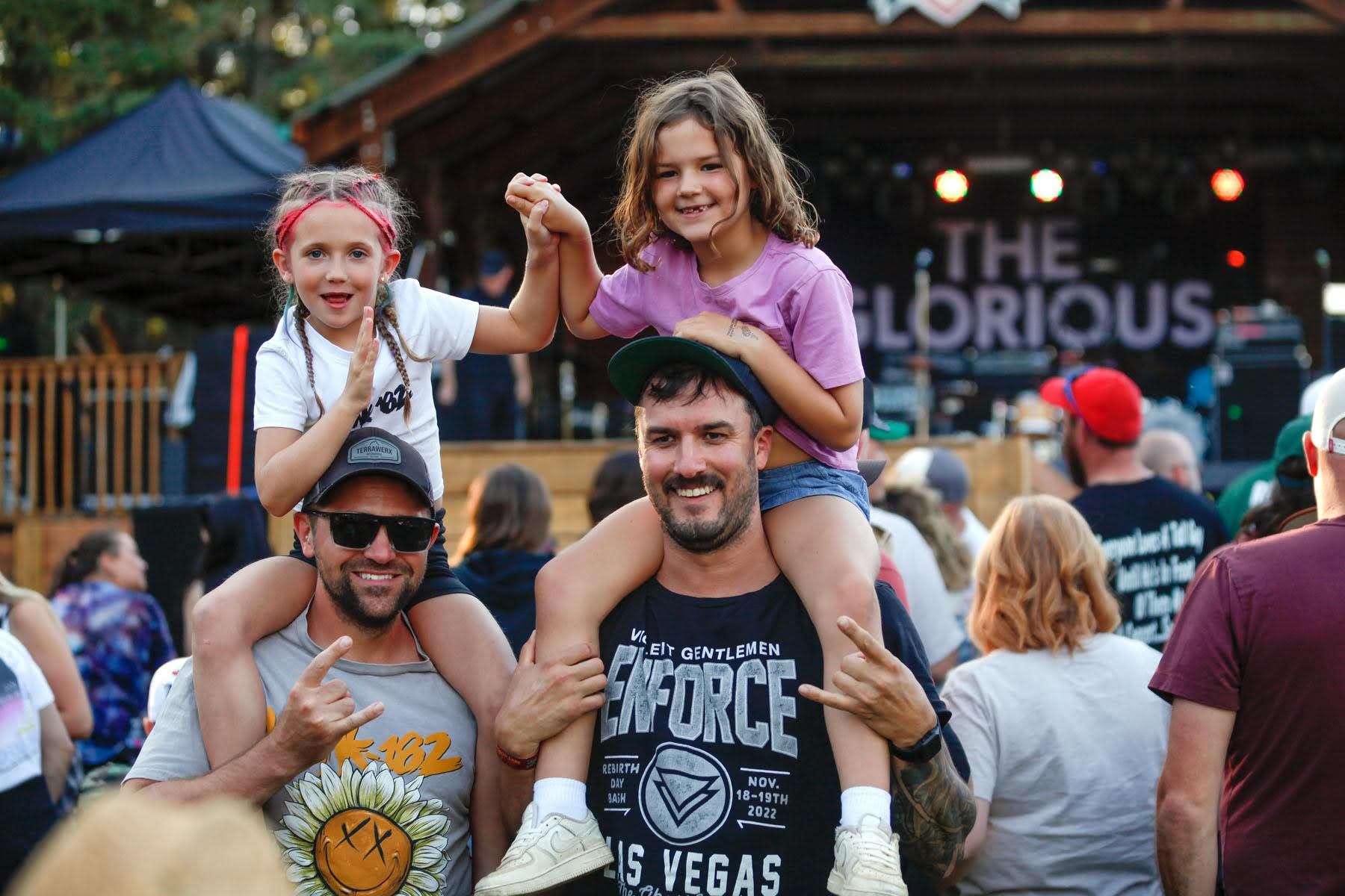 Adults carrying kids on their shoulders while enjoying an outdoor concert at Pigeon Lake.