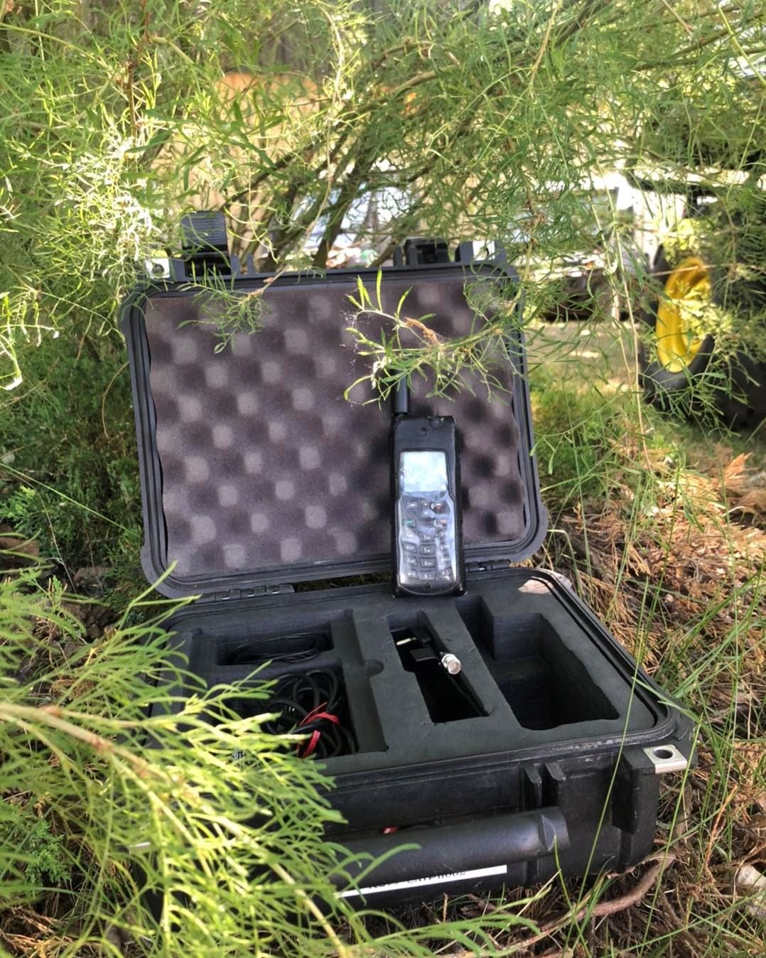 Motorcycle helmet case open in grass with a mobile phone and remote inside.