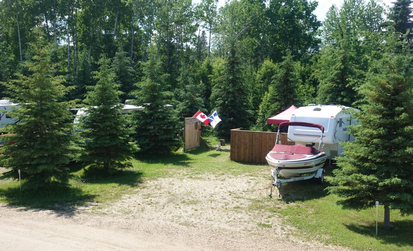 RVs and a boat in treed RV lots. A Candian flag waves in the breeze.
