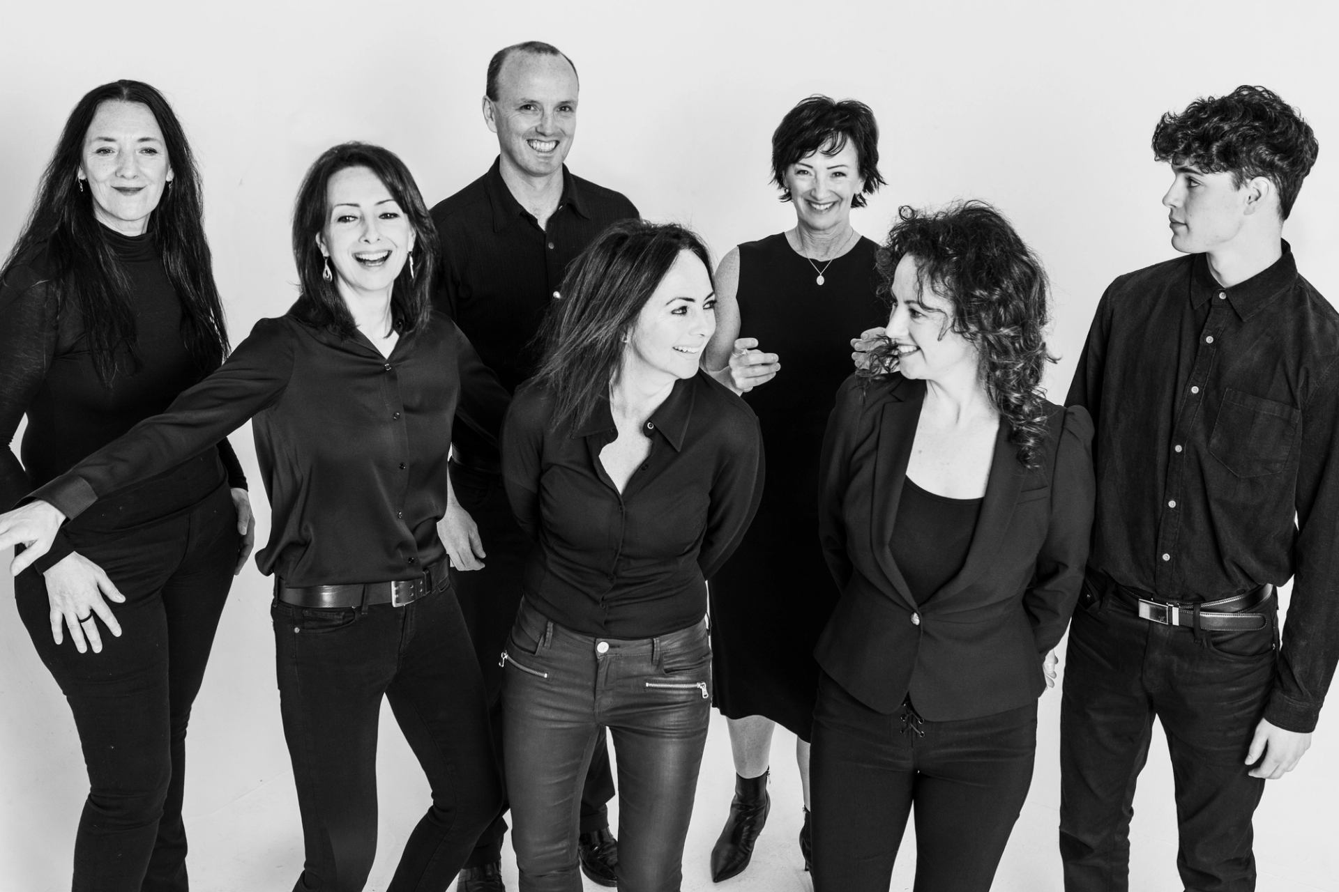Group of people in black clothing standing together in a studio, facing each other.