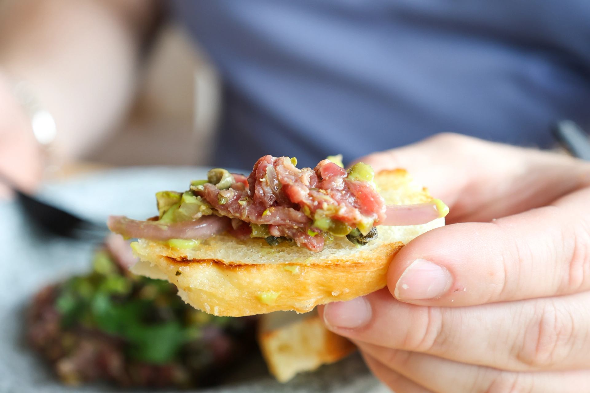 Hand holding toasted bread topped with fresh tuna tartare and herbs.