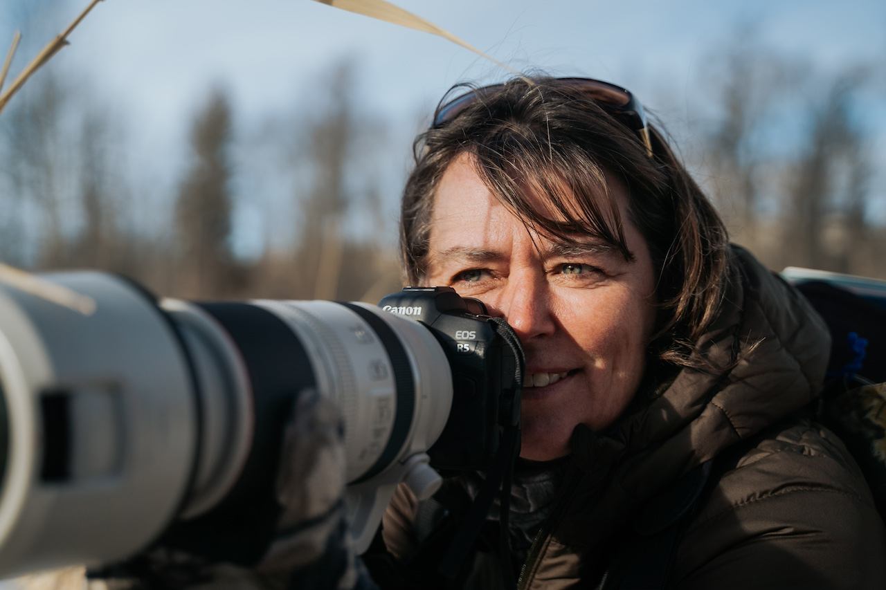 A photographer aims a large telephoto lens while focusing on a subject.