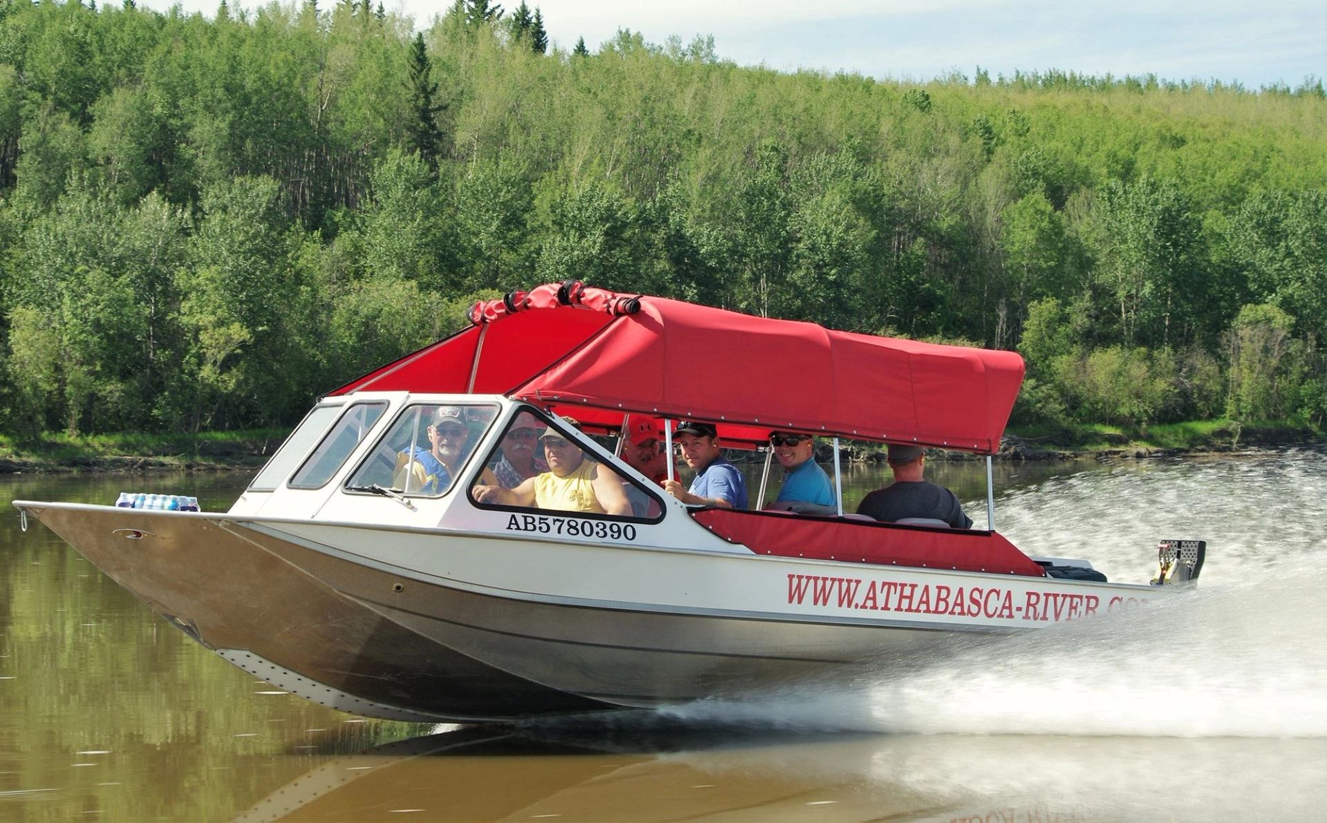A boat full of passengers speeding down the river on a sunny day.