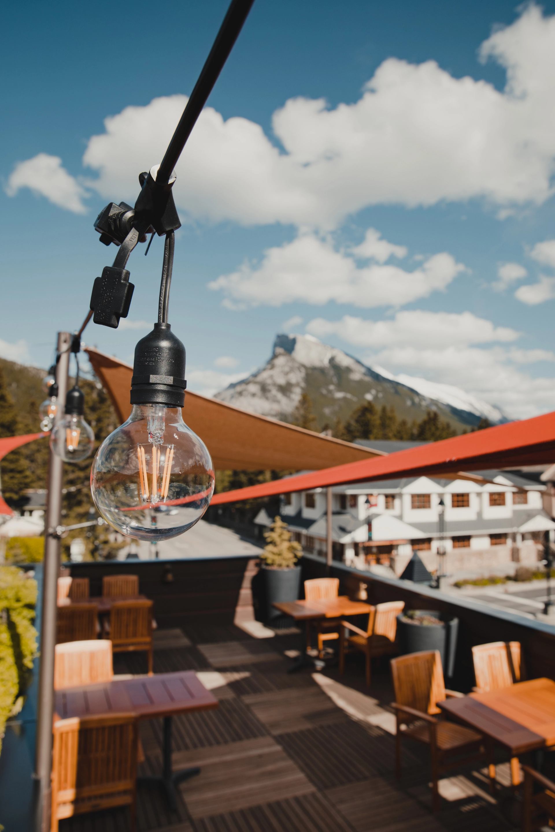 Rooftop patio with string lights and dining sets, overlooking a snow-capped mountain under a blue sky.