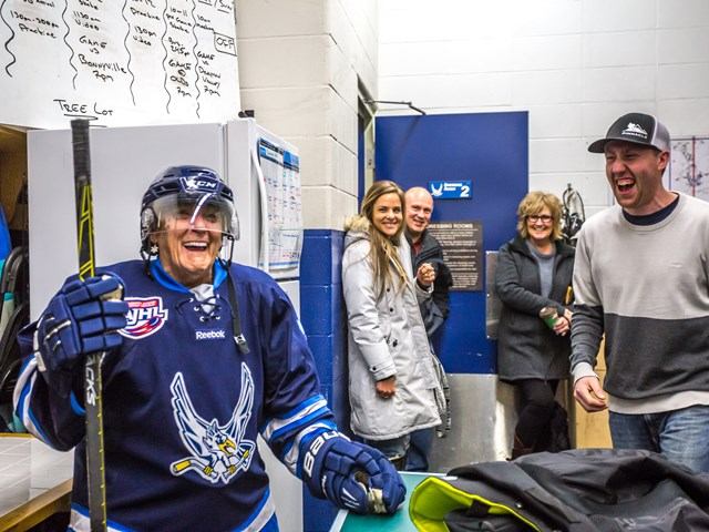 Hockey player in uniform stands near a table with people gathered in the background.