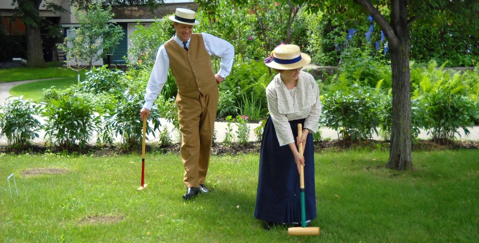 A game of croquet being played by two individuals dressed in period attire.