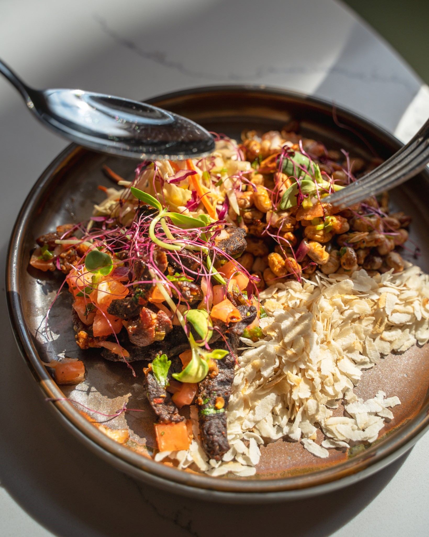 Restaurant bowl with leafy greens, shredded cabbage, beans, and vegetables on a plate.