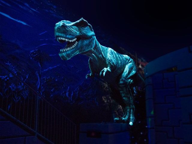 Dinosaur model with open mouth lit in blue beside stairs and railing.