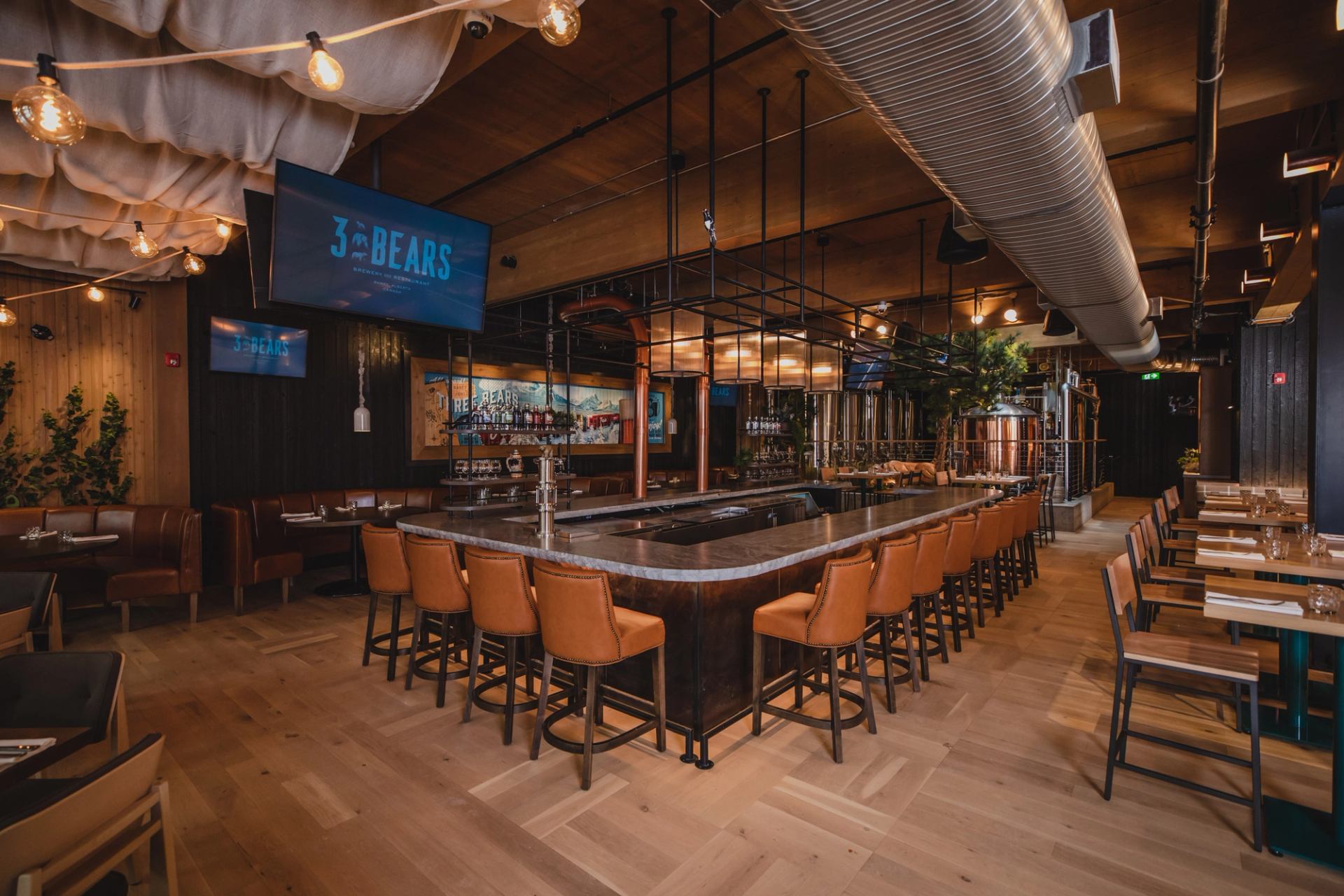 Interior of the "3 Bears" restaurant with a long central bar, orange stools, booth seating, and industrial-chic decor.