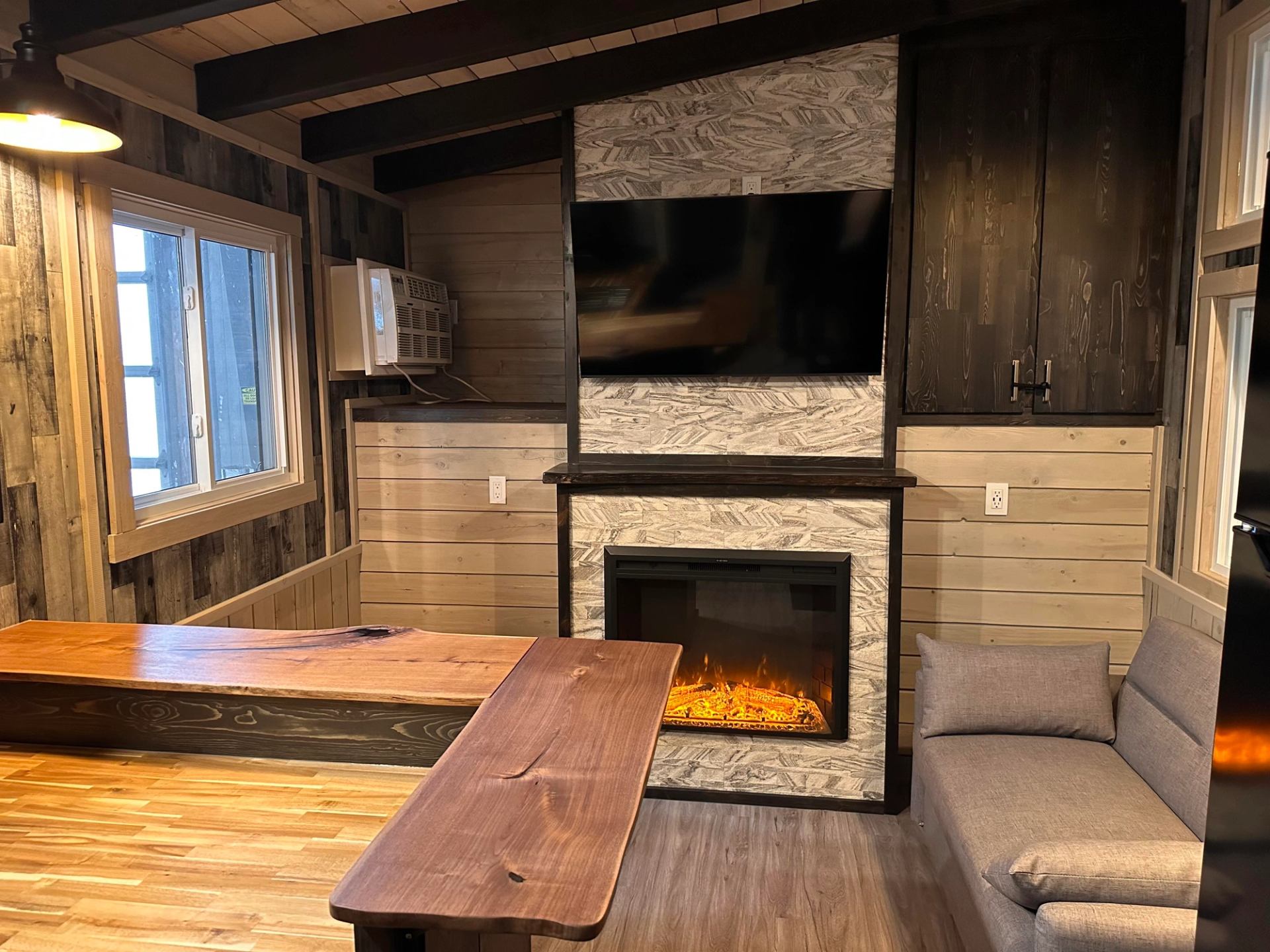 Wood-panelled room with television, electric fireplace, grey sofa and wooden counter.