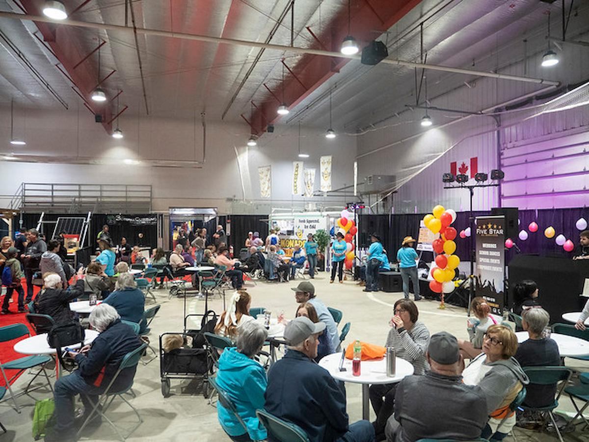 Crowd gathers around tables with balloons in the background