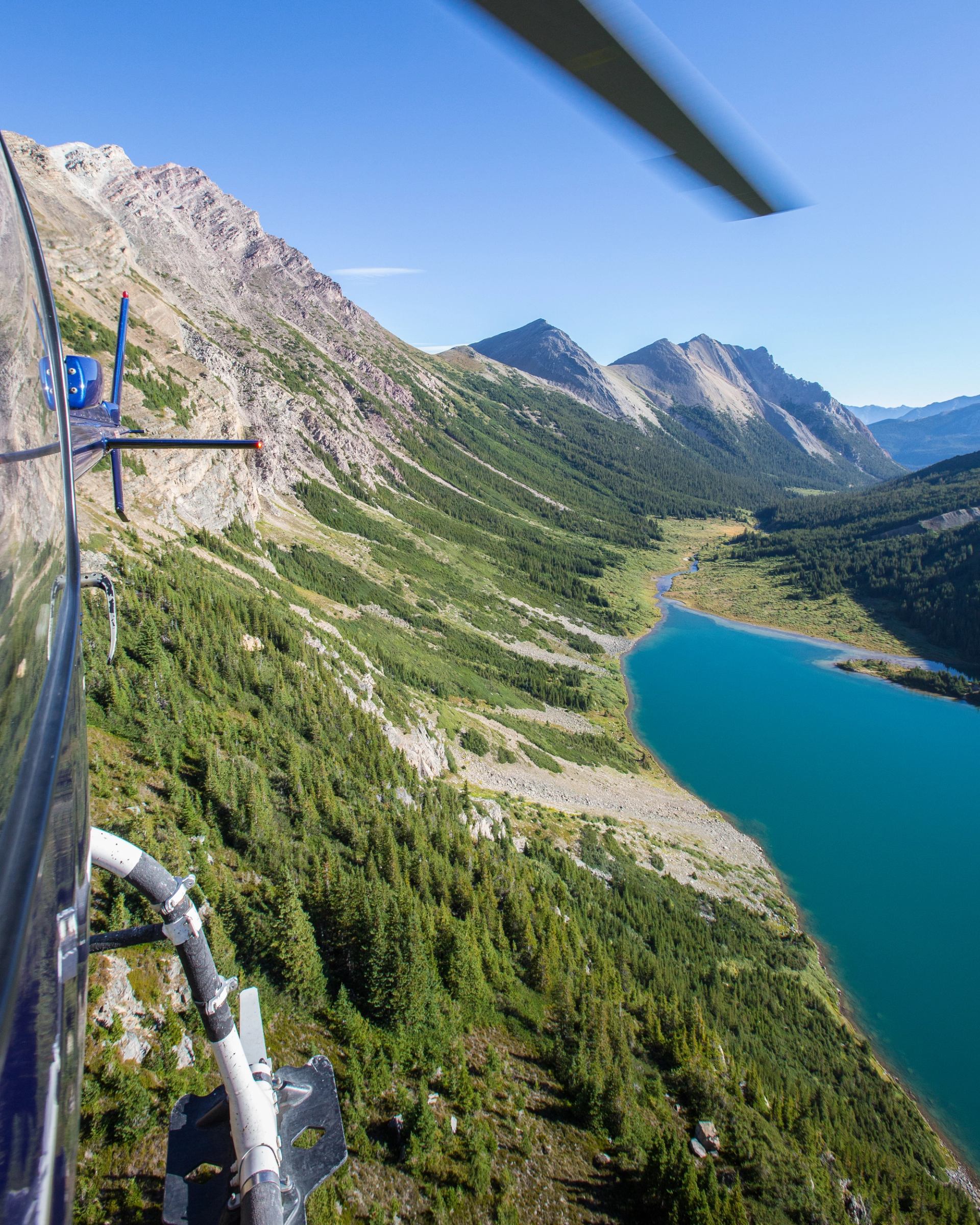 Aerial view from a helicopter over a turquoise lake and mountain valley.