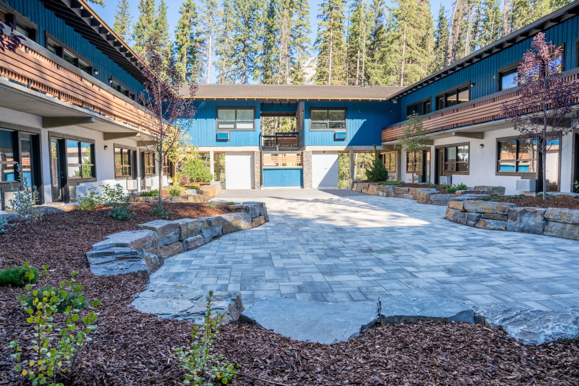 Courtyard at The Dorothy Motel with blue buildings and forest backdrop.