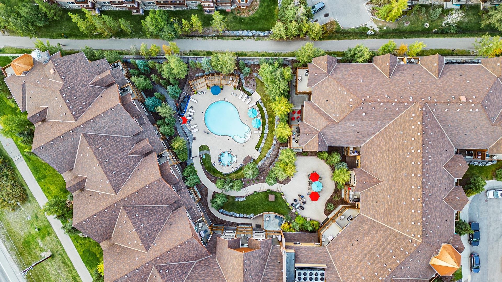 This is an aerial view of a resort with a pool area, hot tubs, and pathways surrounded by trees.