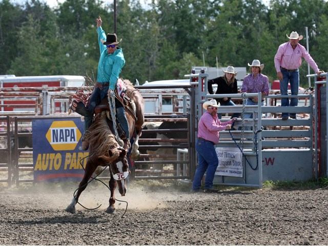 A man with his hand in the air riding a bucking horse.