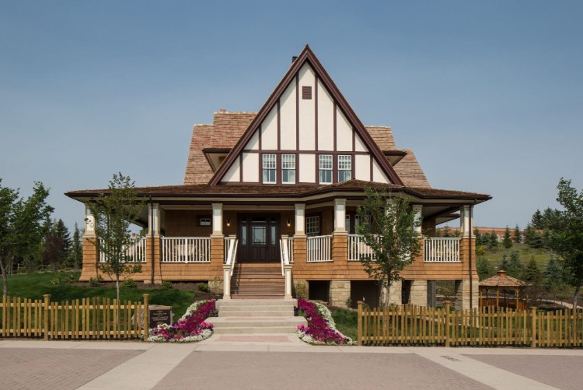 Two-storey Tudor-style house with large front porch, wooden fence and landscaped garden