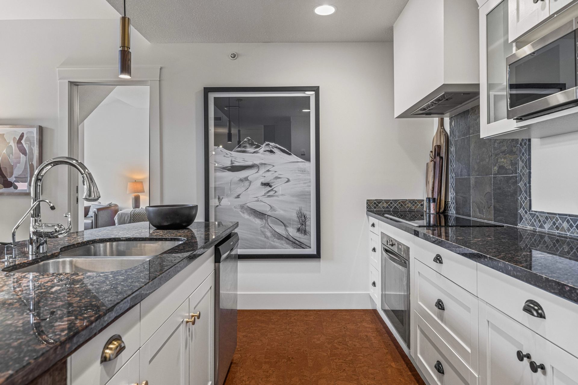 Modern kitchen with dark countertops, stainless appliances and large framed mountain photograph.