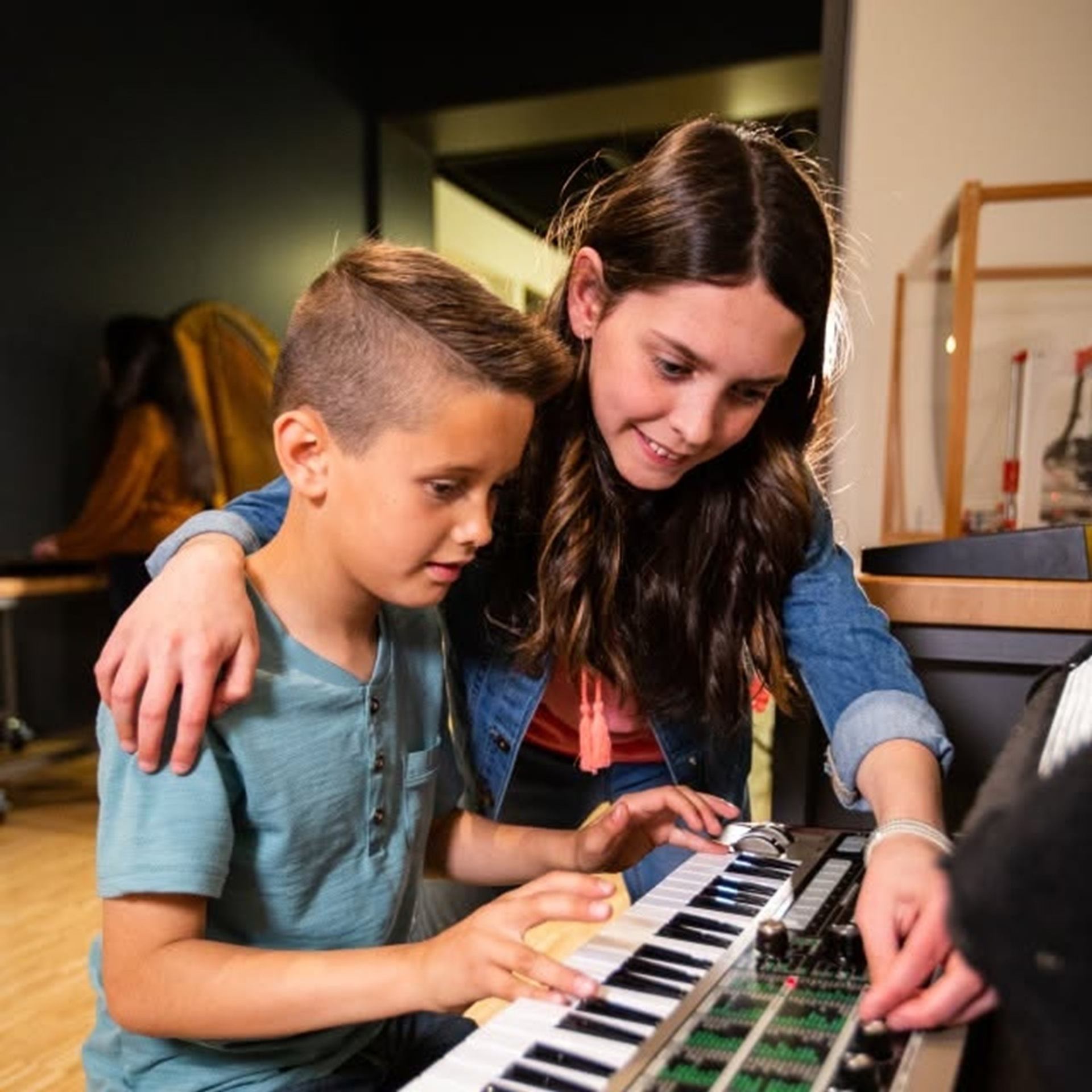 Children use a keyboard and sound mixer while an adult adjusts controls.