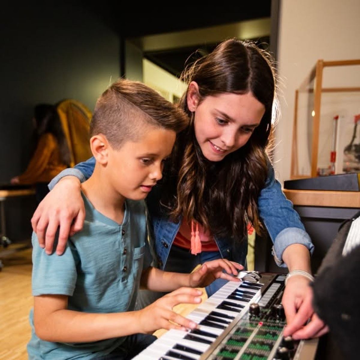 Children use a keyboard and sound mixer while an adult adjusts controls.