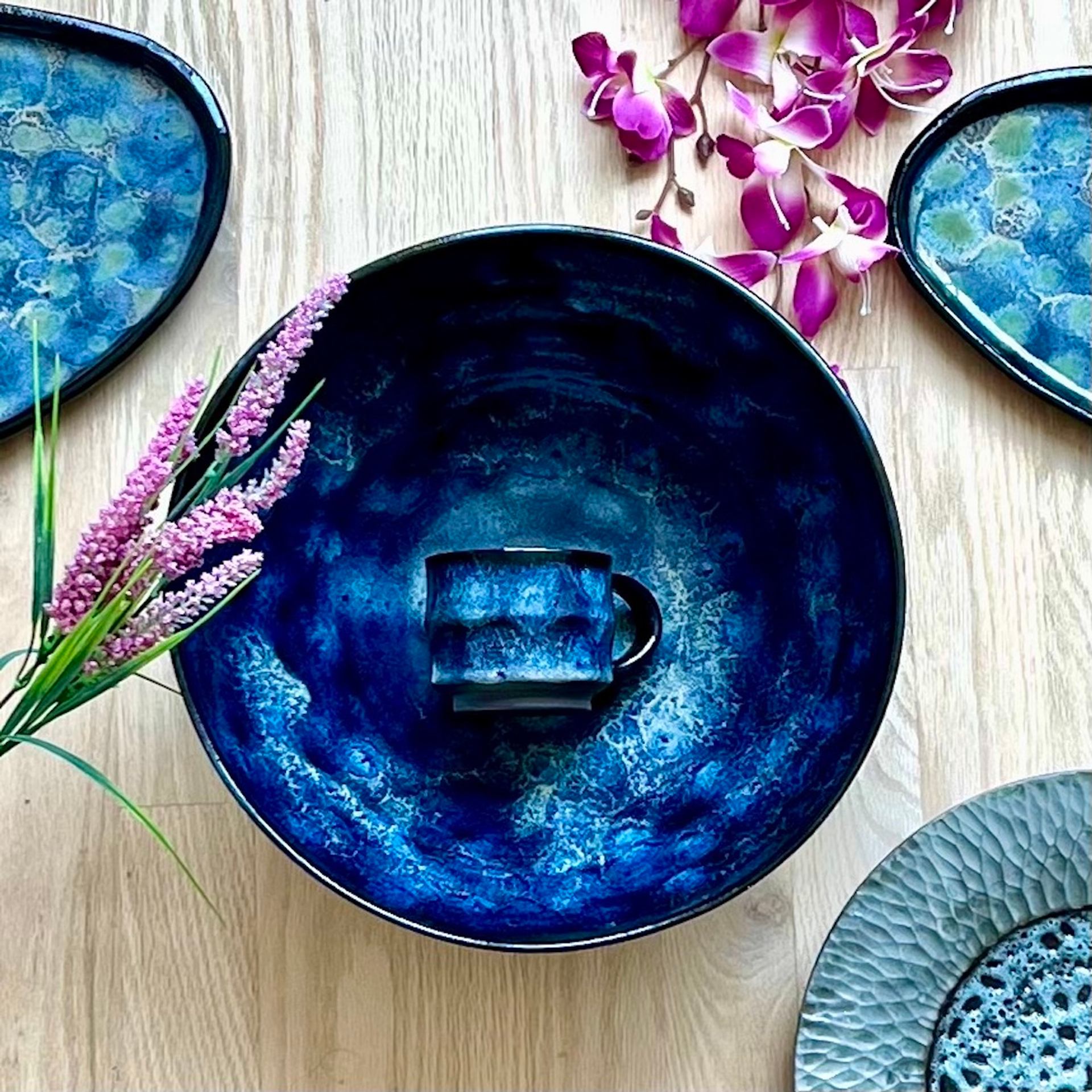 Blue ceramic bowl and cup on wood surface with flowers and matching plates.