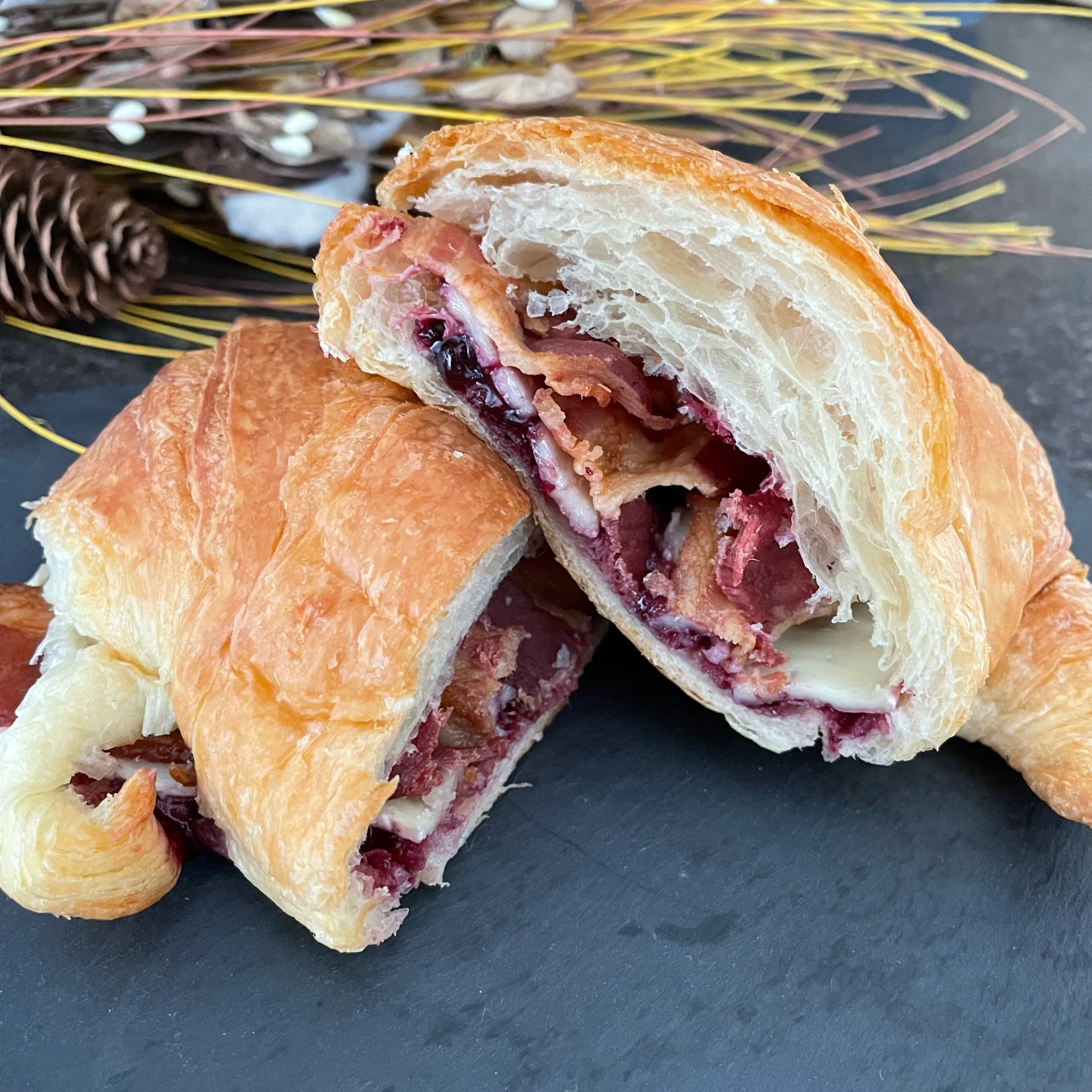 Halved croissant on slate board showing bacon, cheese and berry filling inside.