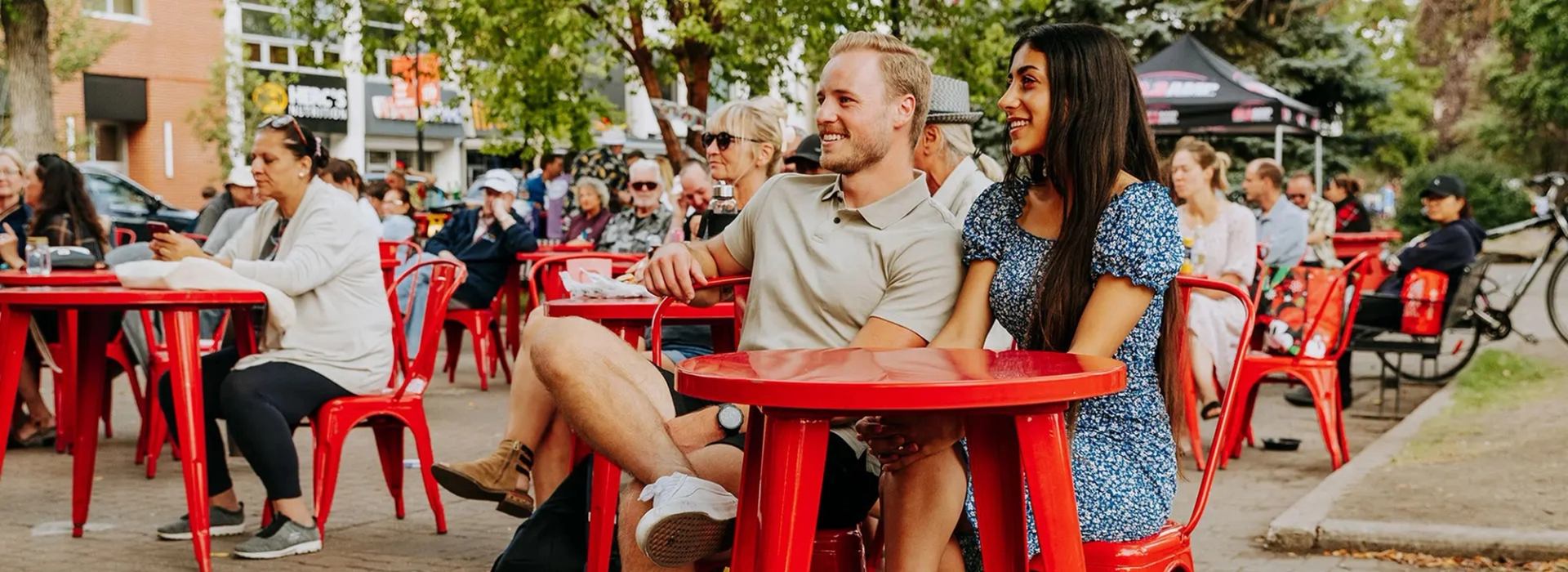 People sit at red patio tables in an outdoor public gathering area.