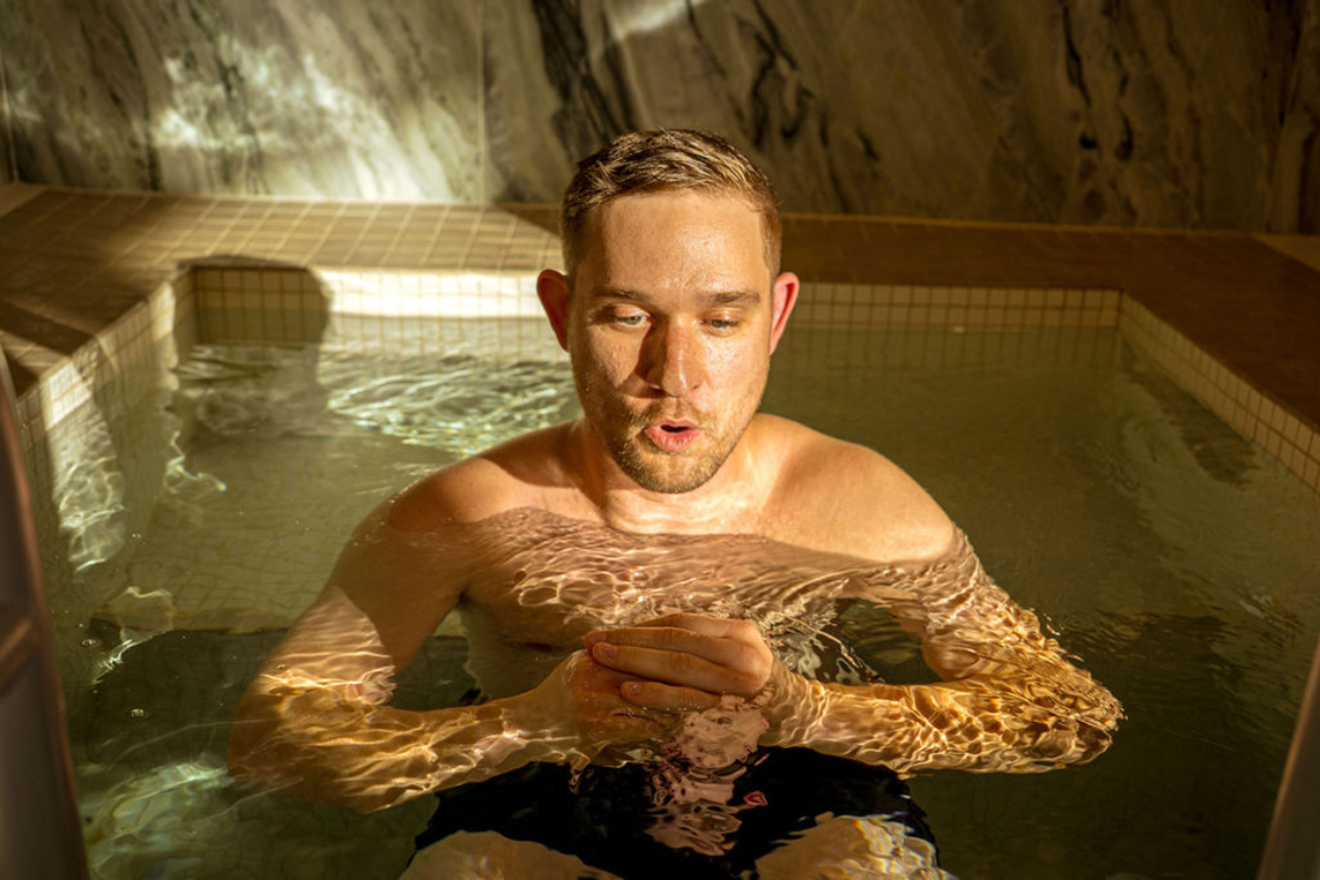 A man with an open mouth, submerged in a warmly lit pool.