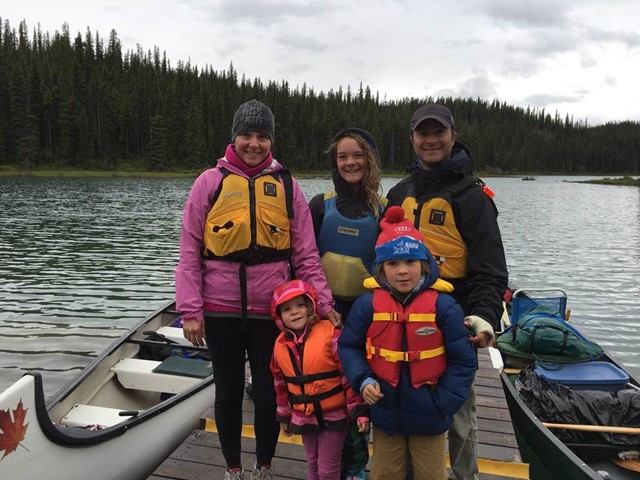 Group stands on dock with canoes, ready for lake adventure at Maligne Lake.