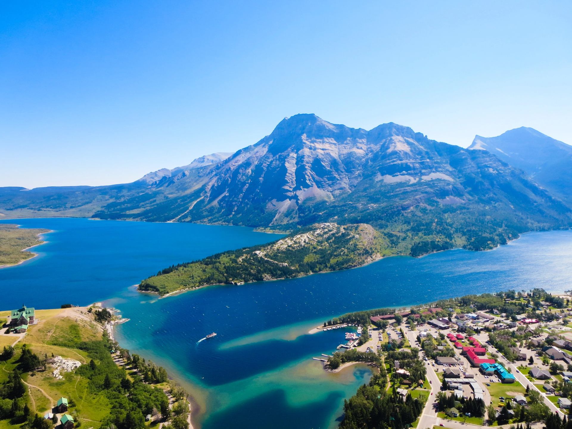 Aerial view of blue lake, forested mountains and small lakeside town with marina.